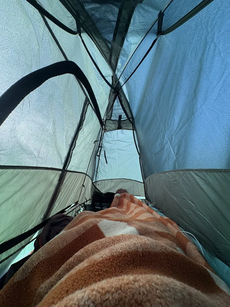 Looking up at the pole structure from inside a tent, a striped fleece blanket in the foreground.