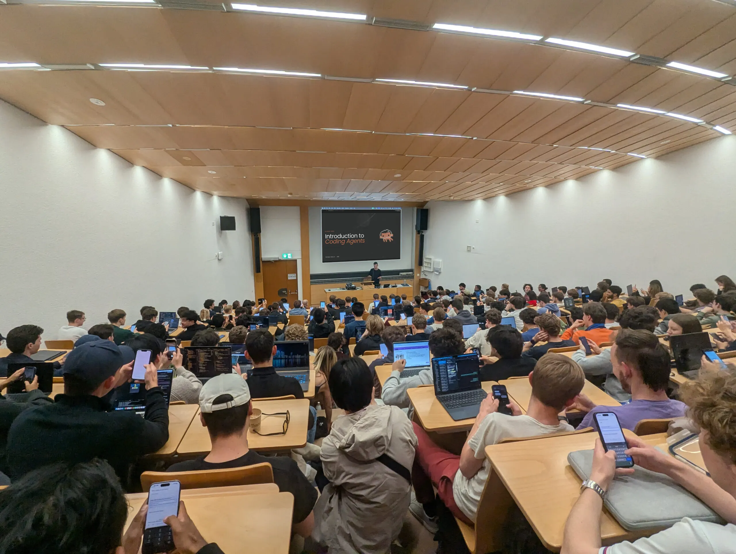 A full lecture hall at ETH seen from the back rows, laptops open, with the title slide"Introduction to Coding Agents" on the screen.
